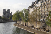 People enjoy the sun next the Notre Dame Cathedral along the Seine river in Paris, Friday, April 19, 2019. Rebuilding Notre Dame, the 800-year-old Paris cathedral devastated by fire this week, will cost billions of dollars as architects, historians and artisans work to preserve the medieval landmark. (AP Photo/Michel Euler)