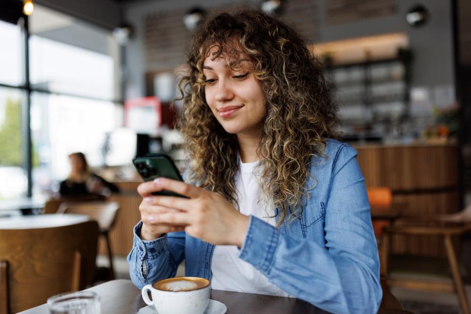 Person with coffee in cafe, looking at phone. 