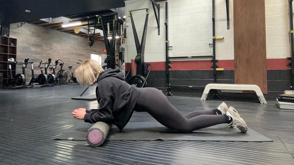  Woman in gym leaning elbows on a foam roller in modified plank position. 