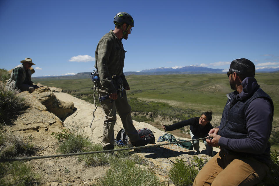 Seasonal biologist Adrian Rouse prepares to practice repelling down a cliff on Wednesday, June 15, 2022 in Cody, Wyo., while Bryan Bedrosian, conservation director at the Teton Raptor Center, supervises. The scientists are monitoring populations of golden eagles, which live on cliff faces in the U.S. West. Nationally, the species is teetering on the edge of decline. (AP Photo/Emma H. Tobin)