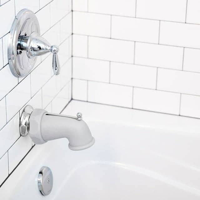 White tiled bathroom with a silver bathtub faucet and shower control