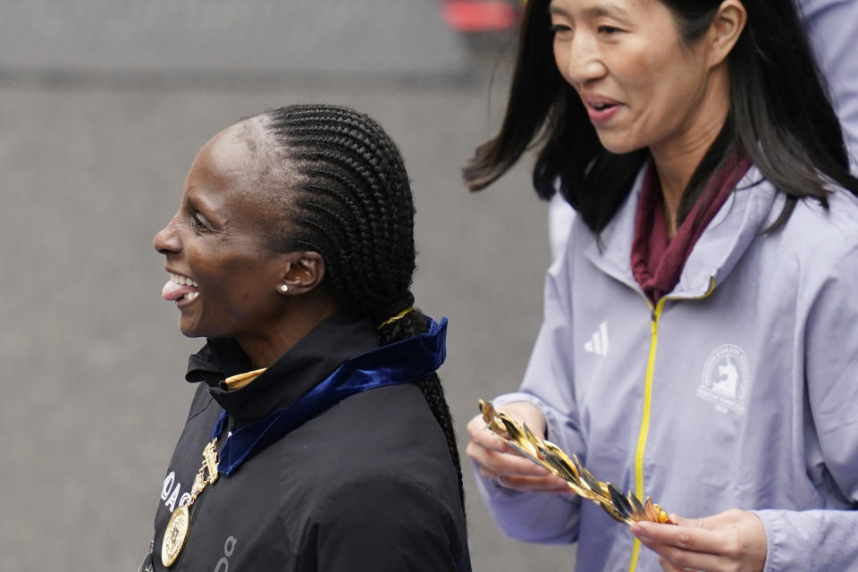 Hellen Obiri, of Kenya, sticks out her tongue prior to the awards ceremony after winning women's division of the Boston Marathon, Monday, April 17, 2023, in Boston. At right is Boston Mayor Michelle Wu. (AP Photo/Charles Krupa)