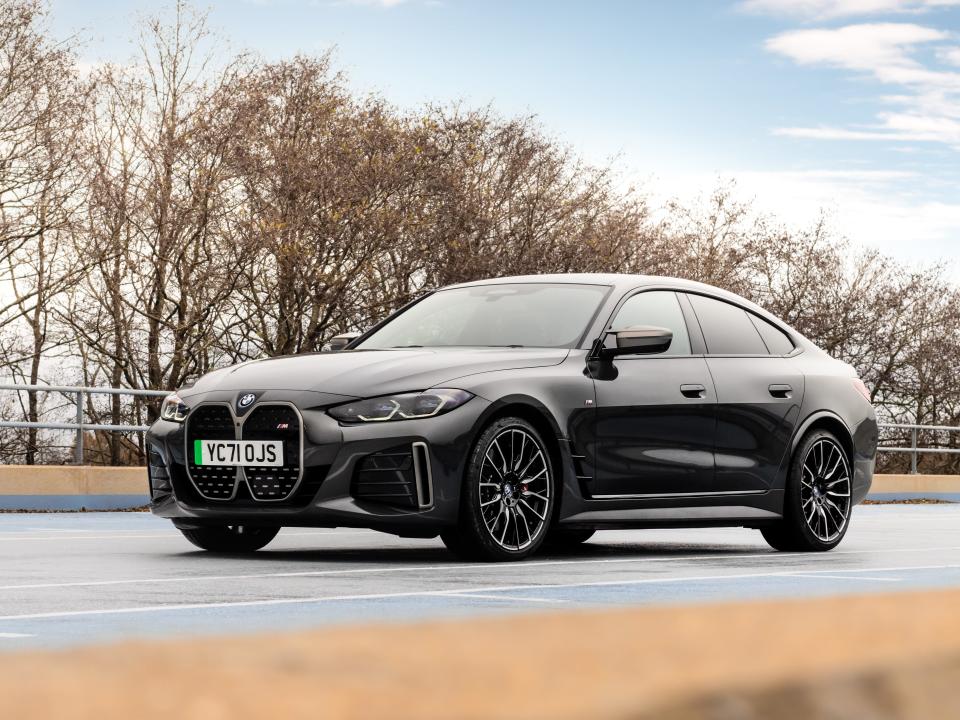 A black BMW i4 M50 on a road with trees in the background.