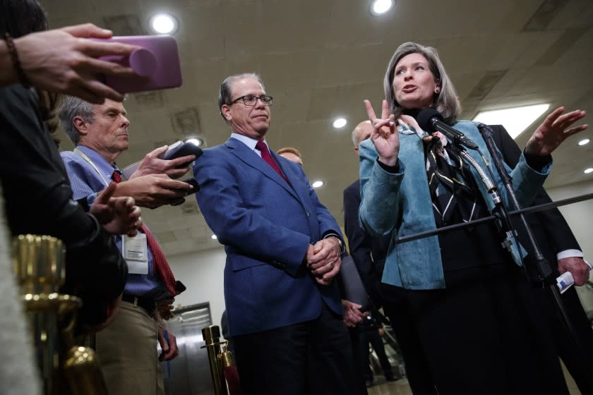 Sen. Mike Braun, R-Ind., left, listens as Sen. Joni Ernst, R-Iowa, speaks to the media during a break in the impeachment trial of President Donald Trump on charges of abuse of power and obstruction of Congress, Friday, Jan. 24, 2020, on Capitol Hill in Washington. (AP Photo/Jacquelyn Martin)