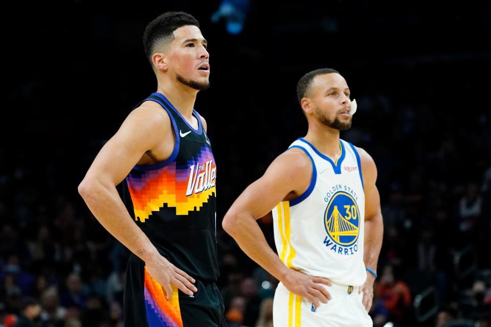 Phoenix Suns guard Devin Booker and Golden State Warriors guard Stephen Curry (30) watch a free throw during the first half of an NBA basketball game, Tuesday, Nov. 30, 2021, in Phoenix.