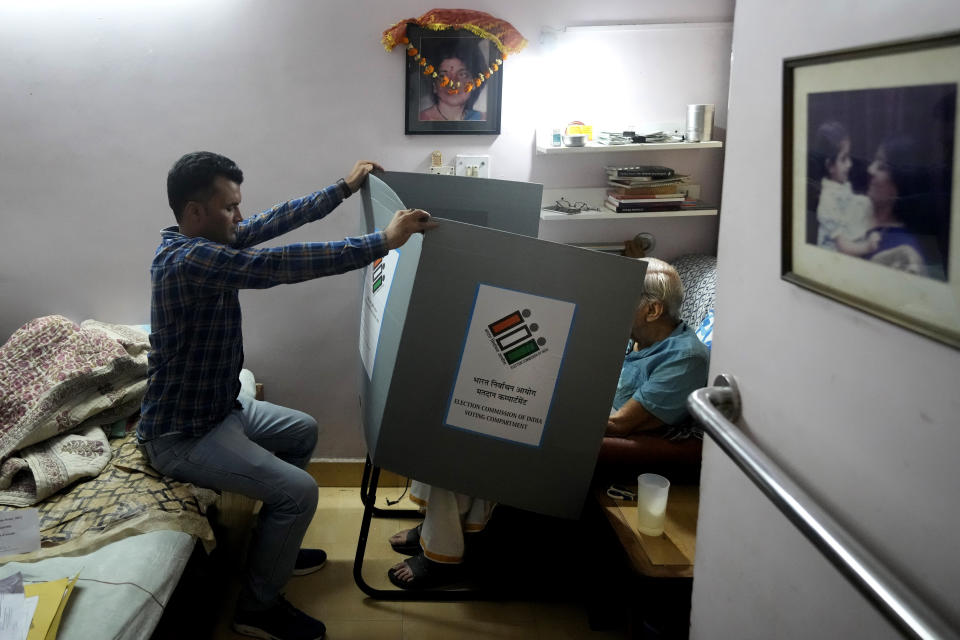 FILE- A polling officer holds a voting compartment as an elderly person casts his vote sitting in his home, in New Delhi, India, Friday, May 17, 2024. (AP Photo/Manish Swarup, File)