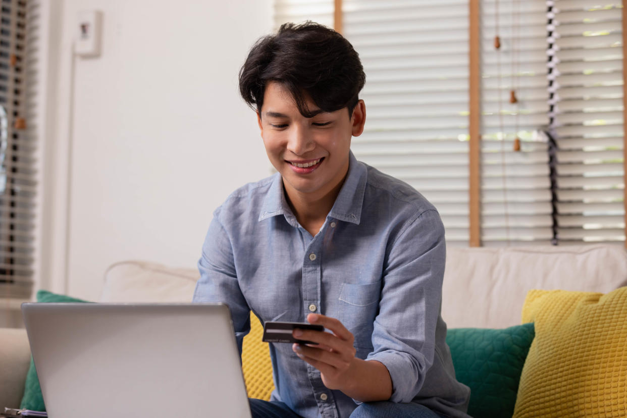 Asian man makes a payment via the internet. On the sofa at home, a shopper shops online using a credit card and a smartphone. The concept of internet shopping.