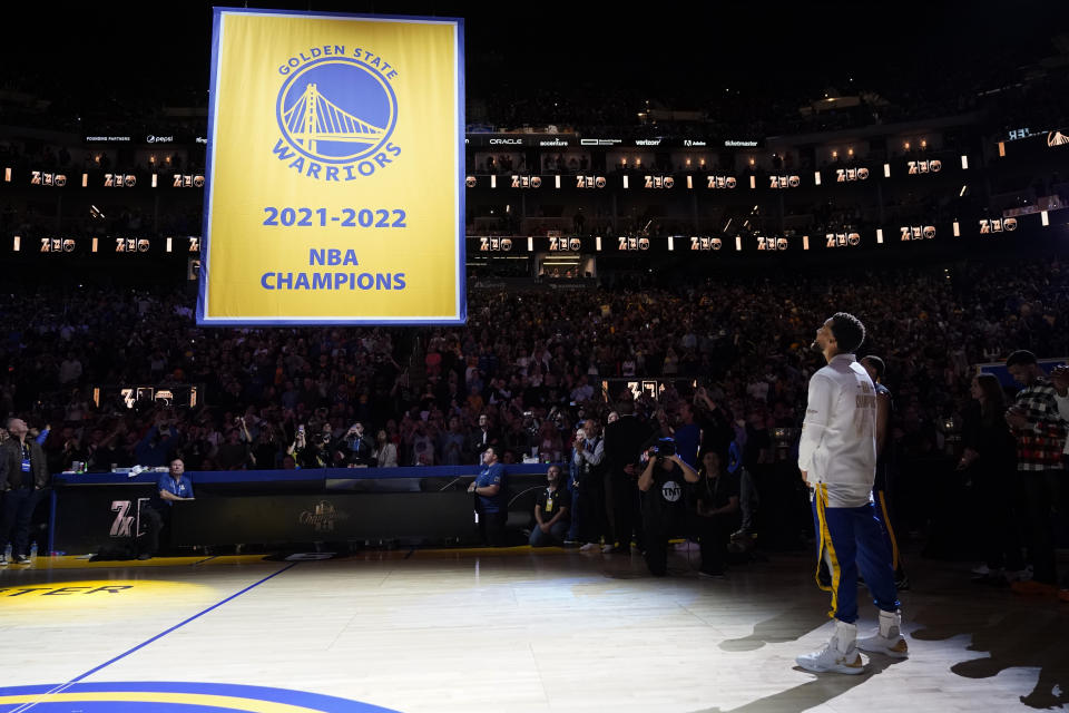 Golden State Warriors guard Stephen Curry, right, watches as the 2021-2022 NBA Championship banner is raised before the team's basketball game against the Los Angeles Lakers in San Francisco, Tuesday, Oct. 18, 2022. (AP Photo/Godofredo A. Vásquez)