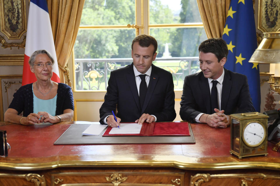 French President Emmanuel Macron (C), flanked by French Transports Minister Elisabeth Borne (L) and French government spokesman Benjamin Griveaux, signs the controversial rail reform, at the Elysee Palace in Paris, on June 27, 2018. / AFP PHOTO / POOL / JULIEN DE ROSA