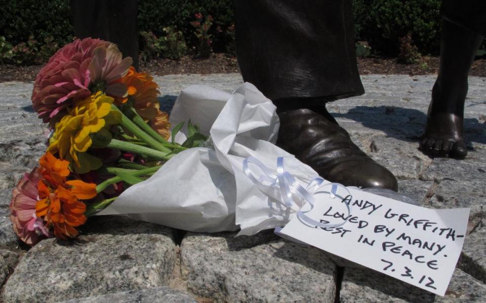 FILE - This July 3, 2012 file photo shows a bouquet of flowers at the foot of a statue of Andy Griffith at Pullen Park in Raleigh, N.C. Tourism in Mount Airy is up since Andy Griffith died July 3, with about 10,400 people visiting the Andy Griffith Museum in July, almost double the 5,400 who visited in July 2011. (AP Photo/Allen Breed, file)