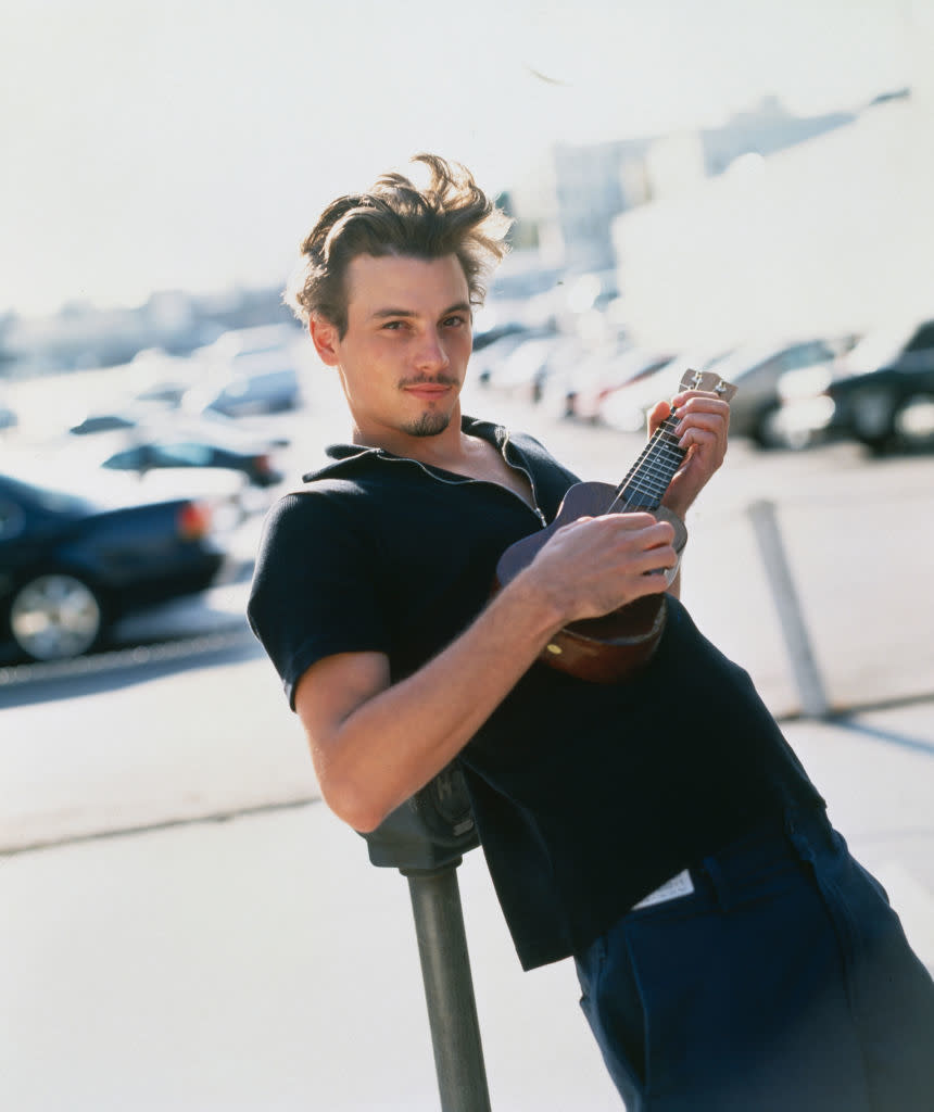 He's slouching and playing a tiny guitar