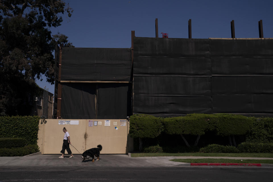 A woman walks her dog past the Jefferson oil drill site enclosed by tall fences in Los Angeles, Wednesday, June 2, 2021. Los Angeles, the second most populous city in the United States, is weighing whether to ban new oil and gas drilling and phase out existing wells. The city council is expected to vote on a measure that would shut down oil and gas fields in the city after a decade of complaints from residents. (AP Photo/Jae C. Hong)