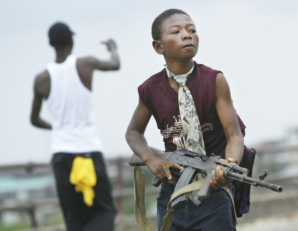 <p>A child Liberian militia soldier loyal to the government walks away from firing on rebel forces across a key bridge while another taunts them July 30, 2003 in Monrovia, Liberia. Sporadic clashes continue between government forces and rebel fighters in the fight for control of Monrovia. (Photo by Chris Hondros/Getty Images) </p>