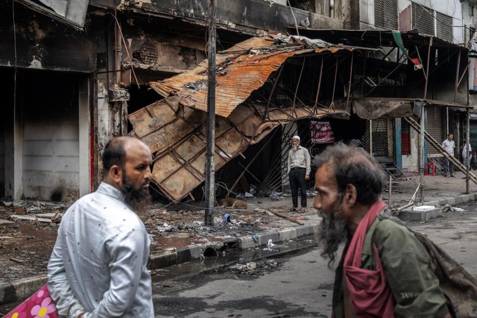 People walk past the Awami League party office and neighbouring buildings that were vandalised and set on fire during the protests (AFP via Getty)