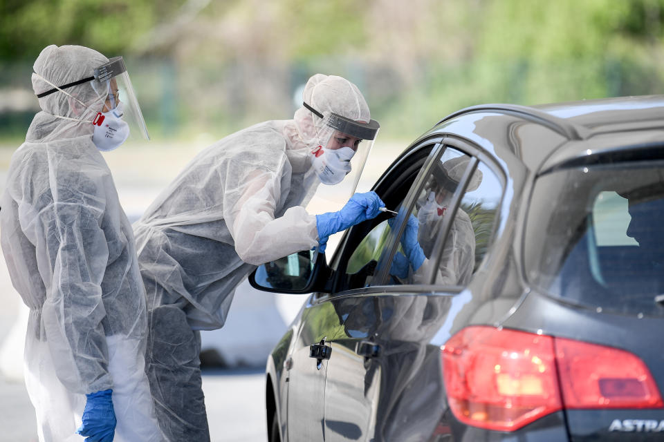 23 April 2020, Berlin: Employees from the Health Department in Mitte hold a swab in a car window on the central fairground in the outpatient corona test facility. The car can now be driven through the Drive-Inn to get a medical smear. For this purpose, the Health Office in Mitte allocates individual time windows by telephone. The tests are to be evaluated by the state laboratory within 24 hours. Photo: Britta Pedersen/dpa-Zentralbild/ZB (Photo by Britta Pedersen/picture alliance via Getty Images)