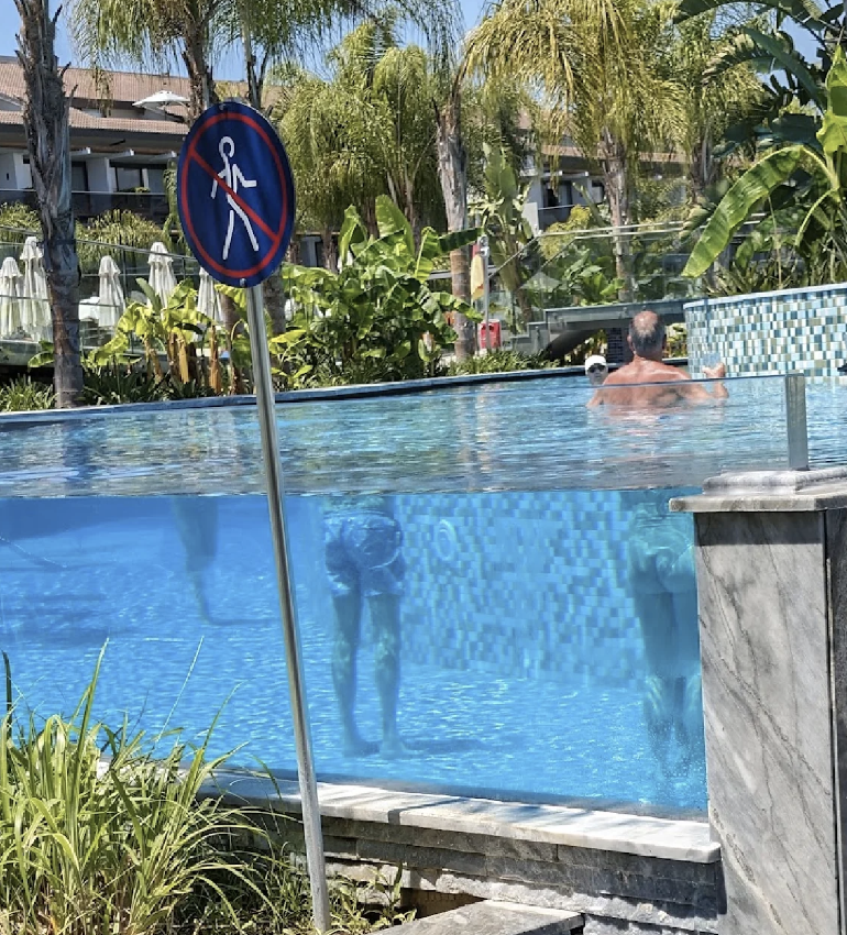 "No diving" sign by a pool with a person swimming in the background