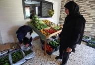 Khadija Shreim stands near her vegetables and fruits stall as a customer buys cucumbers in Houla village