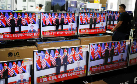 A shopkeeper walks past a set of TV's broadcasting a news report on summit between the U.S. and North Korea, in Seoul, South Korea, June 12, 2018. REUTERS/Kim Hong-Ji/Files