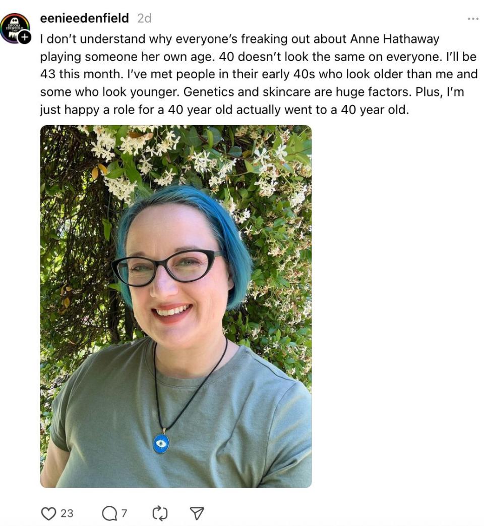 A person with glasses and blue hair smiles in front of flowering bushes. The text discusses how 40 looks different for everyone and mentions genetics and skincare