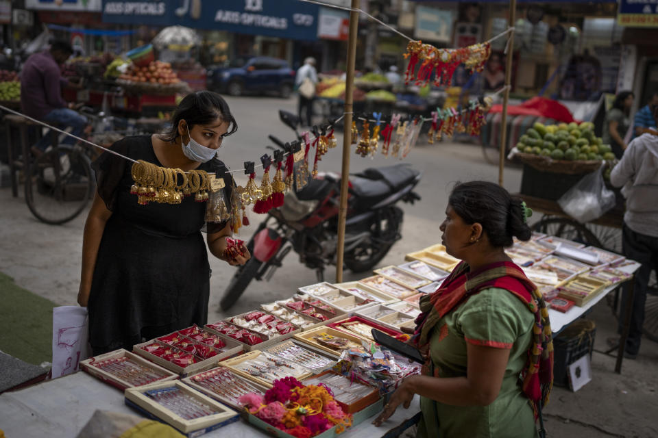 A woman wearing masks as a precaution against coronavirus shops for artificial jewelry from a roadside vendor in New Delhi, India, Thursday, Aug. 11, 2022. The Indian capital reintroduced public mask mandates on Thursday as COVID-19 cases continue to rise across the country. (AP Photo/Altaf Qadri)