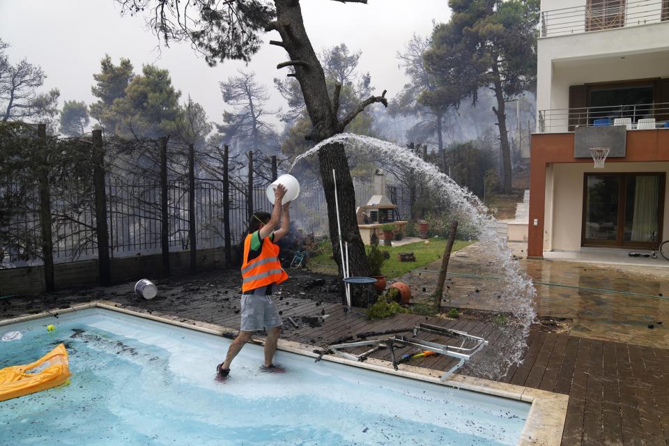 A man throws water from a swimming pool as the fire approaches his house in Ippokratios Politia village, about 35 kilometres (21 miles) north of Athens, Greece, Friday, Aug. 6, 2021. Thousands of people fled wildfires burning out of control in Greece and Turkey. (AP Photo/Thanassis Stavrakis)