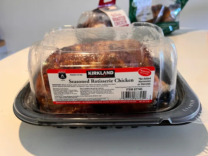 A Costco rotisserie chicken sits on a white table with Kirkland label in front