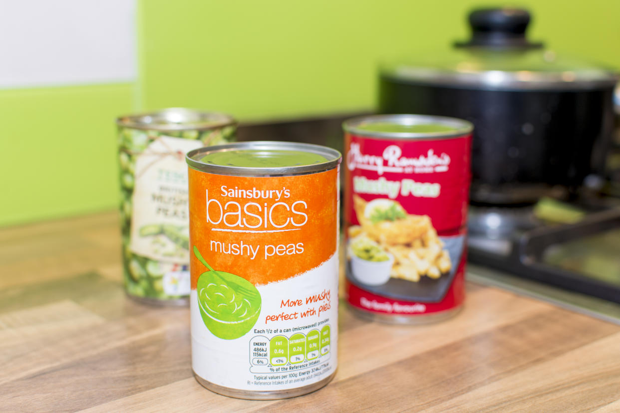 Poole, UK - September 5, 2016: A tin can of Sainsbury's basics (the cheapest range) mushy peas in a kitchen environment. Behind that is a choice of Tesco British Mushy Peas (mid-range) or Harry Ramsden's (leading brand) Mushy Peas. Labels include the brand name, product and nutrional information. 