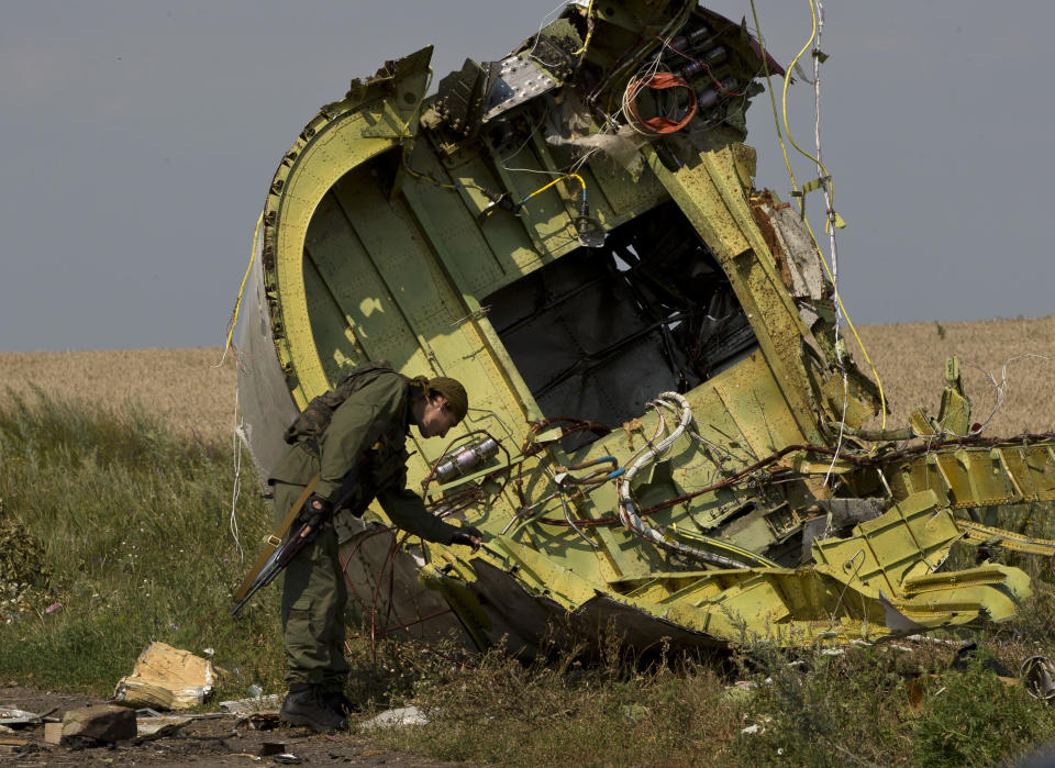 FILE - In this July 22, 2014 file photo, a pro-Russian rebel touches the MH17 wreckage at the crash site of Malaysia Airlines Flight 17, near the village of Hrabove, eastern Ukraine. Five years after a missile blew Malaysia Airlines Flight 17 out of the sky above eastern Ukraine, relatives and friends of those killed are gathering Wednesday July 17, 2019, at a Dutch memorial to mark the anniversary. (AP Photo/Vadim Ghirda, File)