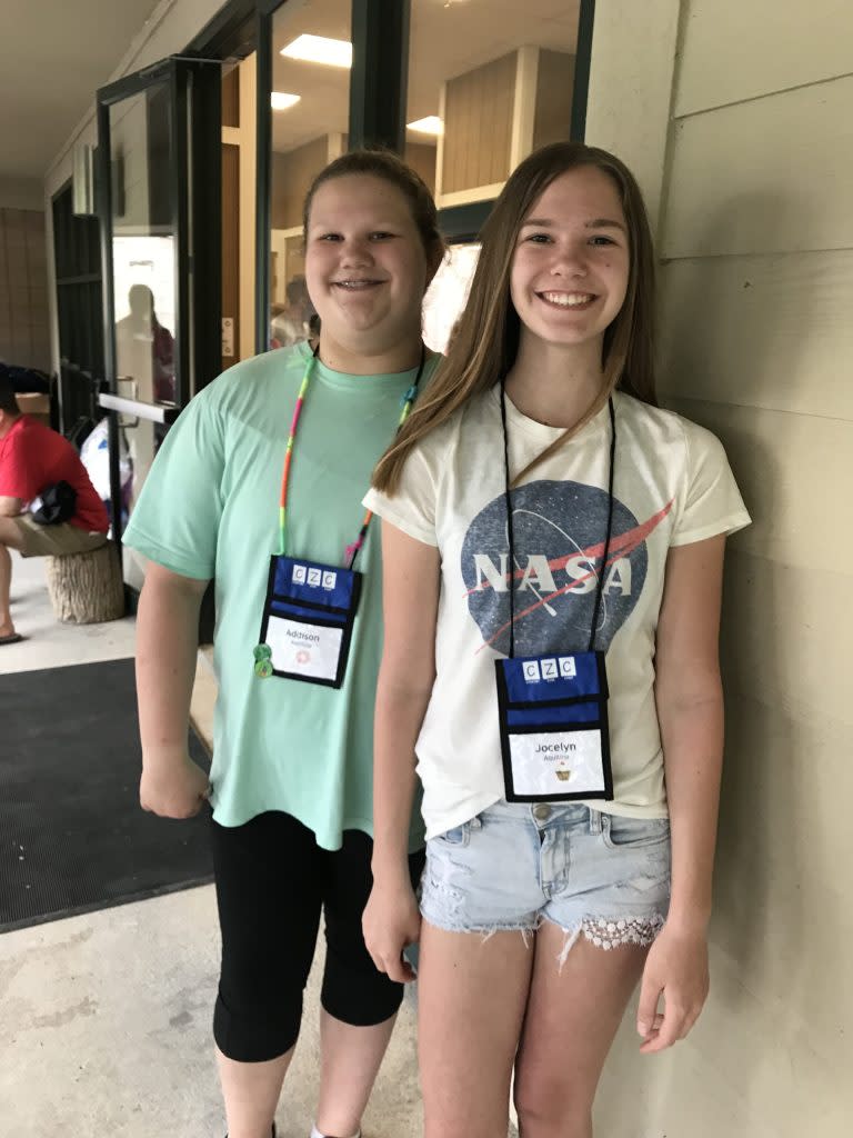 Two sisters stand next to each other to pose for a photo. Both are wearing lanyards around their necks.