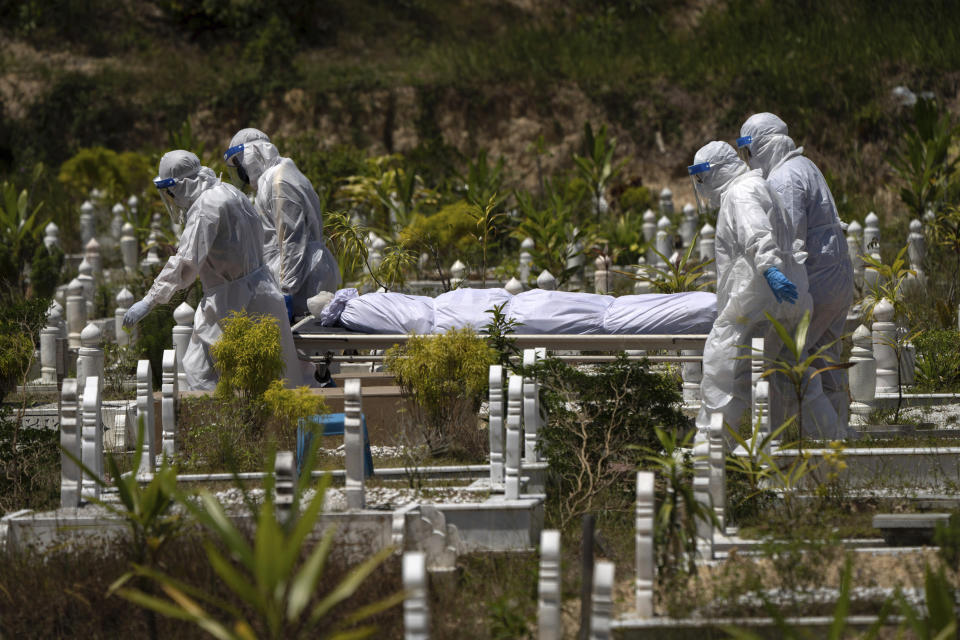 In this Feb. 5, 2021, file photo, workers wearing personal protective equipment (PPE) carry the body of a victim of the coronavirus disease at a Muslim cemetery in Gombak on the outskirts of Kuala Lumpur, Malaysia. Images of bodies burning in open-air pyres during the peak of the pandemic in India horrified the world in May, but in the last two weeks Malaysia and two other Southeast Asian nations have surpassed India’s peak per capita death rate as a new coronavirus wave tightens its grip on the region. (AP Photo/Vincent Thian, File)