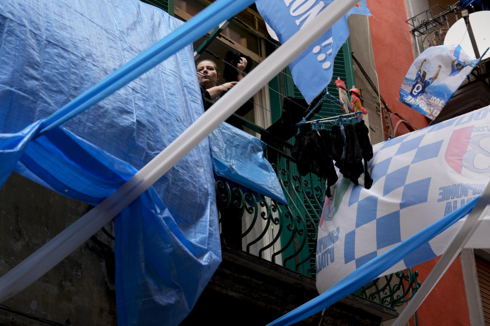 A woman hangs out the laundry among banners and writings in support of Napoli soccer team, in downtown Naples, Italy, Tuesday, April 18, 2023. It's a celebration more than 30 years in the making, and historically superstitious Napoli fans are already painting the city blue in anticipation of the team's first Italian league title since the days when Diego Maradona played for the club. (AP Photo/Andrew Medichini)