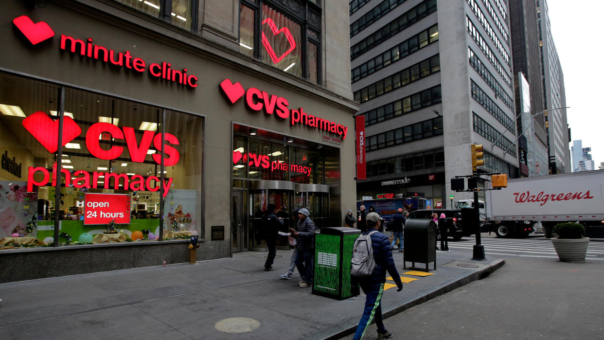  Photo of the outside facade of a CVS Pharmacy in new york city as people walk past and a walgreens delivery truck drives by in the background. 