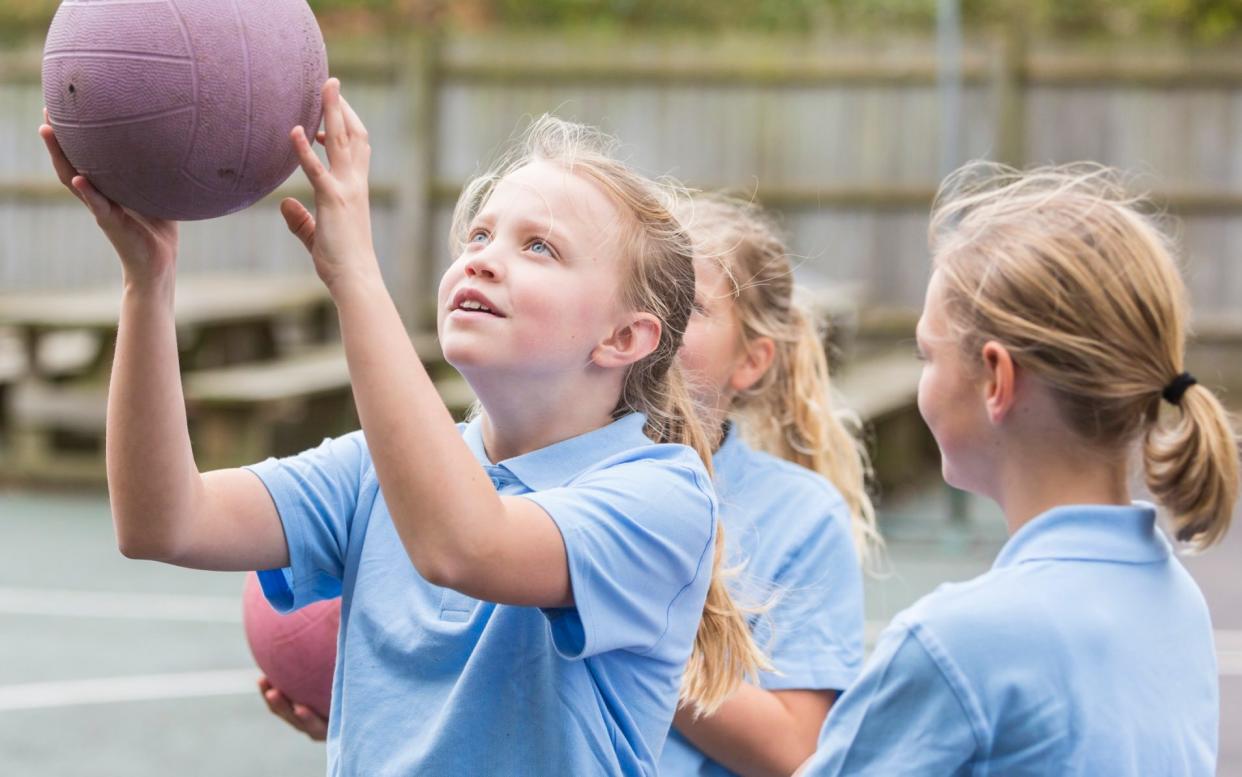 Girls in school uniform playing netball in the school yard - Getty