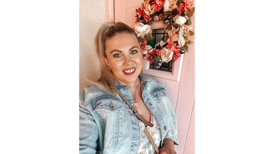 woman taking a selfie in front of a pink door with a wreath