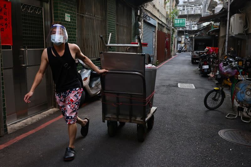 A person wearing a protective face masks pushes his stall ready for the reopening of a night market in Taipei