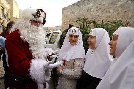 Israeli-Arab Issa Kassissieh wears a Santa Claus costume as he speaks with nuns during the annual Christmas tree distribution by the Jerusalem municipality in Jerusalem's Old City December 21, 2017. REUTERS/Ammar Awad