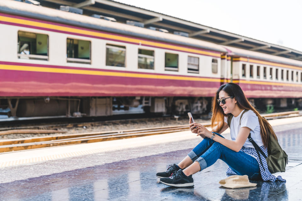 A young woman checks her smartphone at a railway station.