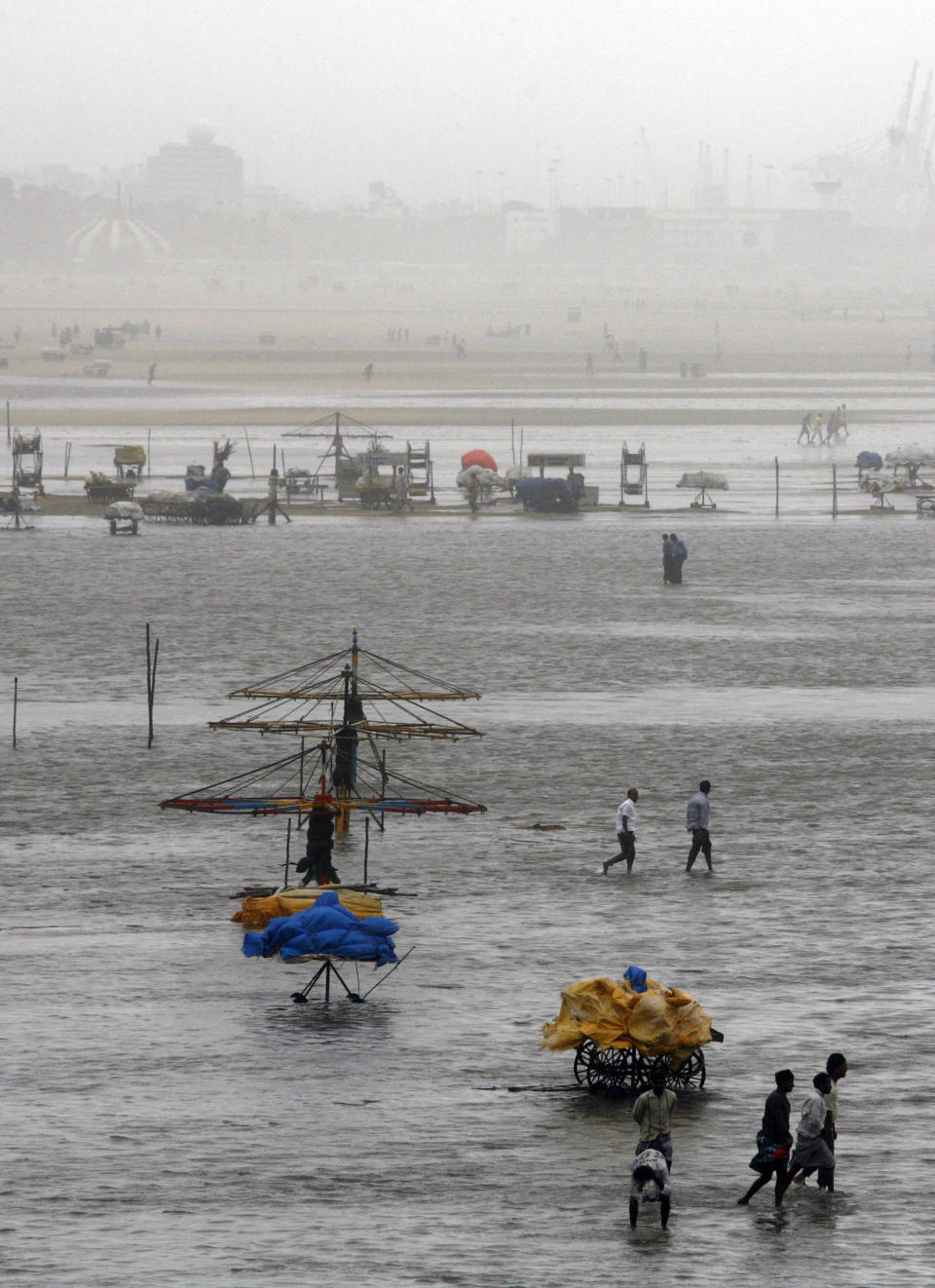 People walk on the Marina beach after the same is flooded with sea water on the Bay of Bengal coast in Chennai, India, Wednesday, Oct. 31, 2012. More than 100,000 people were evacuated from their homes Wednesday as a tropical storm approached southern India from the Bay of Bengal, officials said. Rain was already lashing the region and strong winds uprooted trees in some places. Weather officials said the storm, with wind speeds of up to 100 kilometers (60 miles) per hour, was expected to reach land later Wednesday. (AP Photo/Arun Sankar K)