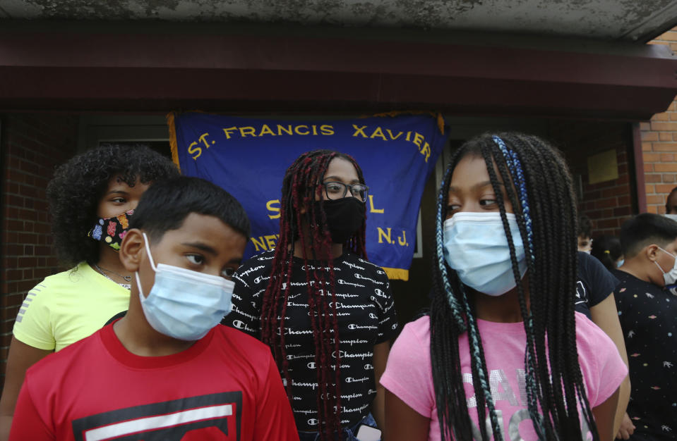 FILE - In this Thursday, Aug. 6, 2020 file photo, Malik Bey, 11, left, stands with his sisters in front of St. Francis Xavier School in Newark, as parents meet to fight the school's permanent closure. Amid the pandemic, more than 200 schools closed for good, and enrollment at the 5,981 remaining schools fell by 6.4% -- or more than 111,000 students – for the 2020-2021 academic year, according to the National Catholic Educational Association. (AP Photo/Jessie Wardarski)