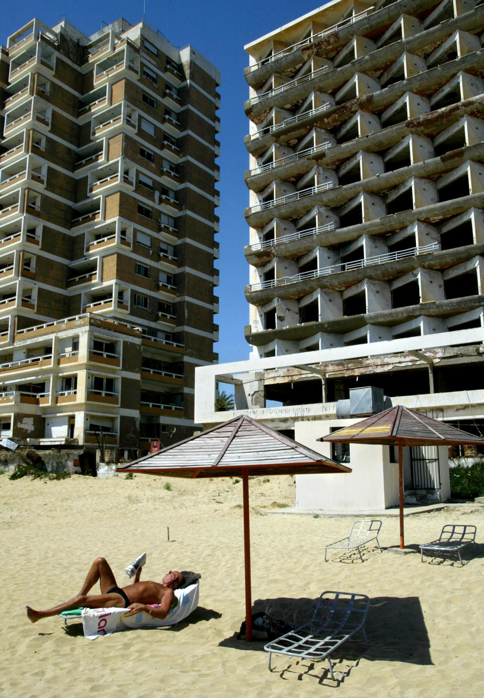 FILE - In this Monday, May 5, 2003 file photo, a tourist reads his book as he sunbathes in front of a destroyed hotel in the Turkish-occupied of abandoned coastal city of Varosha, in southeast of the island of Cyprus. Time virtually stopped in 1974 for the Mediterranean tourist playground of Varosha. When Turkey invaded Cyprus in the wake of a coup by supporters of union with Greece, thousands of residents fled, and chain-link fences enclosed a glamorous resort that it’s said once played host to Hollywood royalty like Elizabeth Taylor. (AP Photo/Petros Karadjias, file)