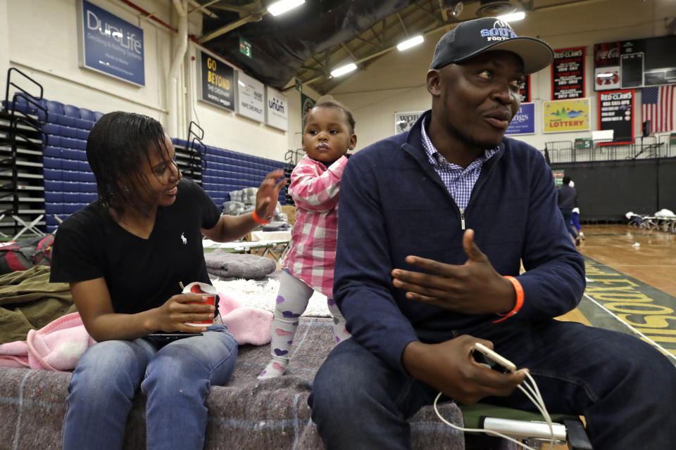 In this June 13, 2019 photo, Prince Pombo speaks about his family's journey as migrants from Africa, at the Portland Exposition Building in Portland, Maine. With him is his wife, Thaiz Neri and their daughter, Heaven. Maine's largest city has repurposed the basketball arena as an emergency shelter in anticipation of hundreds of asylum seekers who are headed to the state from the U.S. southern border. Most are arriving from Congo and Angola. (AP Photo/Elise Amendola)