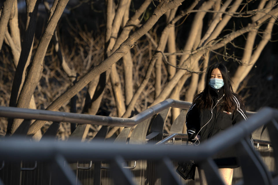 A woman wearing a face mask to protect against the spread of the coronavirus walks along a street during the morning rush hour in Beijing, Wednesday, Dec. 30, 2020. Beijing has urged residents not to leave the city during the Lunar New Year holiday in February, implementing new restrictions and mass testings after several coronavirus infections last week. (AP Photo/Mark Schiefelbein)