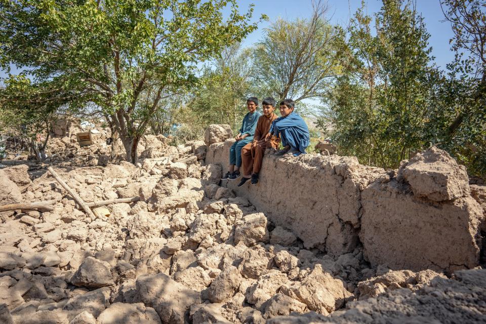 Thirteen-year-old Abdul (sitting in middle in brown shalwar kameez) sits with two friends as they look over his destroyed house in Karnil Wardaka village, Zinda Jan District, western Afghanistan.