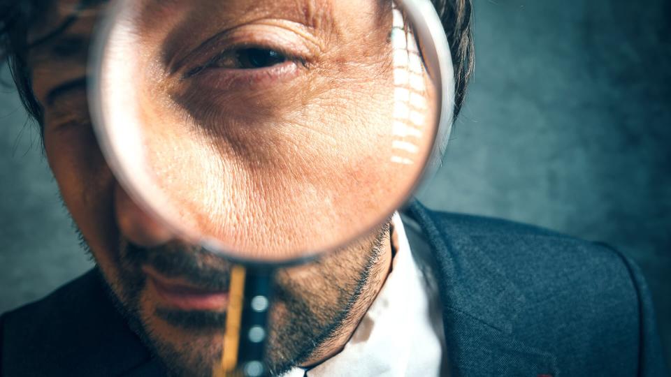 Enlarged eye of tax inspector looking through magnifying glass, inspecting offshore company financial papers, documents and reports.