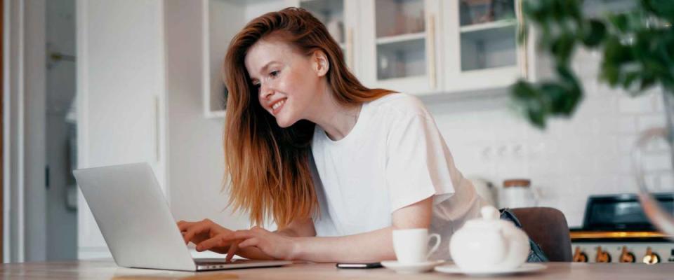 A satisfied housewife types an email message to the bank on her laptop. Applies for a mortgage loan online at the bank. The woman is a young red-haired European-looking student.