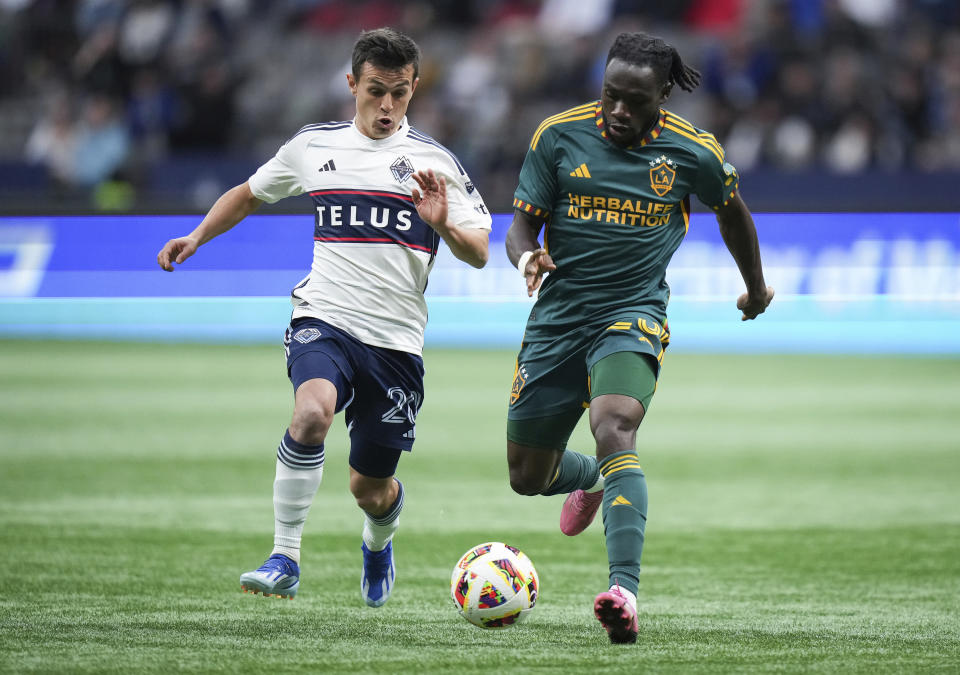 Vancouver Whitecaps' Andres Cubas, left, and LA Galaxy's Joseph Paintsil vie for the ball during the first half of an MLS soccer match Saturday, April 13, 2024, in Vancouver, British Columbia. (Darryl Dyck/The Canadian Press via AP)