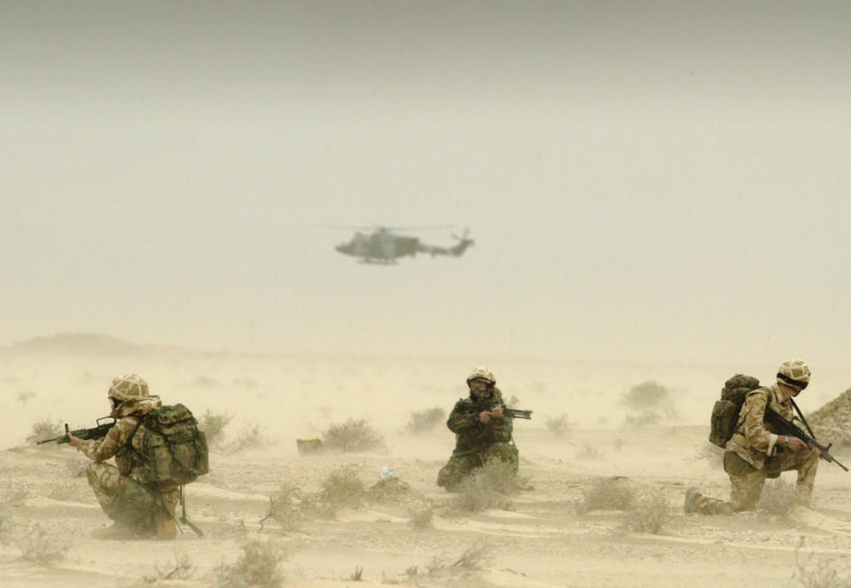 Soldiers of Britain's 3 Army Air Corps crouch in a sandstorm in the desert, with a helicopter flying overhead.