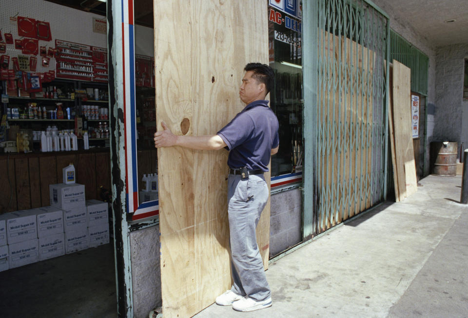 FILE - Chae Son Han, who works in an auto parts store in Los Angeles' Koreatown, takes down protective boards outside his store on April 19, 1993. Business was almost back to normal after verdicts in the Rodney King civil rights trail. (AP Photo/Nick Ut, File)