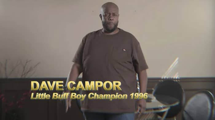 a man wears a t-shirt and jeans. he is mid-sentence, and there is a lower third that reads "dave campor, little buff boy champion 1996"