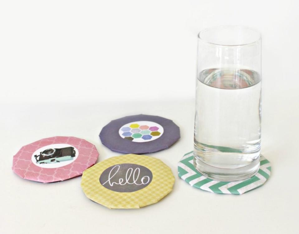 Four handmade cardboard coasters, one with a water glass on top.